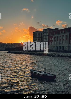 Ein Boot schwimmt im Wasser in der Nähe eines Gebäudes. Die Sonne untergeht und strahlt ein warmes Licht auf die Szene Stockfoto