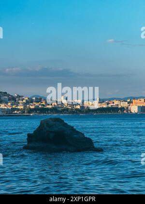Ein großer Felsen befindet sich im Meer in der Nähe einer Stadt. Der Himmel ist klar und das Wasser ist ruhig Stockfoto