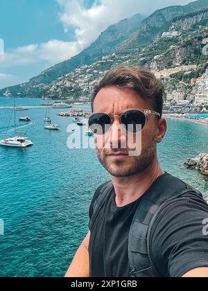 Ein Mann mit Sonnenbrille und schwarzem Hemd macht ein Selfie vor einem Wasser Stockfoto