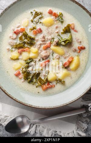 Fleischige, cremige Zuppa toscana Suppe mit italienischer Wurst, Speck und Gemüse aus der Nähe auf dem Teller auf dem Tisch. Vertikale Draufsicht von oben Stockfoto