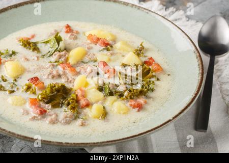 Italienische traditionelle Suppe Zuppa Toscana mit Würstchen, Grünkohl, Kartoffeln und Speck in Nahaufnahme auf einem Teller auf dem Tisch. Horizontal Stockfoto