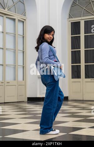 Ein Teenager in blauer Jeans und gestreiftem Hemd posiert für ein Foto. Sie hält eine blaue Tasche in der Hand. Das Bild hat eine lässige und entspannte Atmosphäre Stockfoto