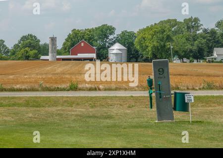 Eine Abschlagbox für Loch Nummer 9 auf einem Golfplatz mit einer Scheune und Silos eines ländlichen Bauernhofs im Hintergrund an einem teilweise bewölkten Tag Stockfoto