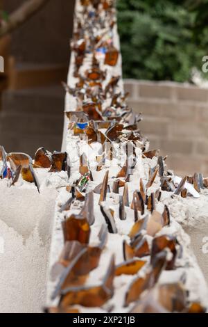 Eine detaillierte Aufnahme von scharfen Glassplittern, die in Beton an einer Wand als Sicherheitsmaßnahme in Gambia platziert sind und Schutz und Barrieren symbolisieren. Stockfoto