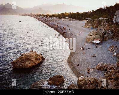 Atemberaubender Blick auf den Strand in Antalya, Türkei, mit Leuten, die den Abend genießen. Die Szene fängt die Mischung aus Natur und menschlicher Ruhe ein. Stockfoto