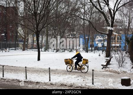 Postbote, der im Januar 2010 mit dem Fahrrad durch das schneebedeckte Berlin-Kreuzberg fuhr. Die Szene symbolisiert Beharrlichkeit und Hingabe trotz widriger Witterungsbedingungen. Stockfoto