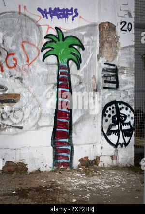 Graffiti mit einer lebendigen Palme und abstrakten Mustern auf einer zerrissenen Stadtmauer, die den Zusammenprall zwischen Natur und Stadtleben symbolisieren. Stockfoto