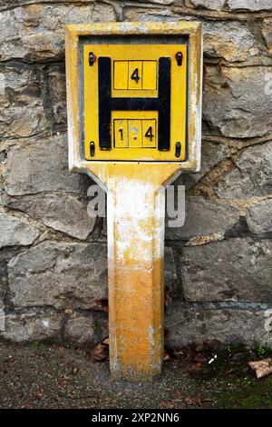 Altes gelbes Schild des Löschwasserhydranten aus Großbritannien. Es ist eine Markierungsplatte, die die Position (Entfernung) und Größe (Durchmesser) des britischen Wassers angibt Stockfoto