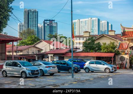 Parkplatz für den Pak Koong Tempel mit modernen Turmblöcken im Hintergrund und älteren flachen Wohnhäusern im Vordergrund. Stockfoto