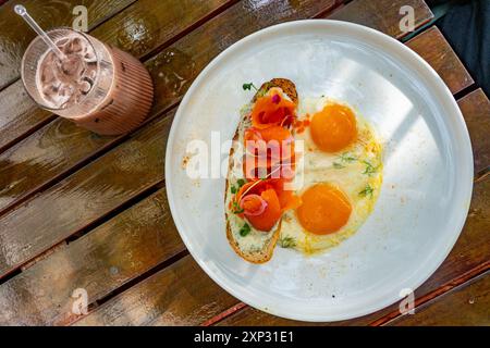 Räucherlachs auf Toast mit Spiegeleiern zum Frühstück mit einem Schokoladen-Milchshake in einem Restaurant während des Urlaubs. Stockfoto