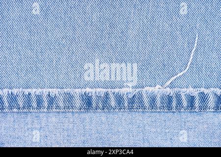 Blaue Jeans Hose mit schäbigem Rand auf jeansstoff Hintergrund, Nahaufnahme, Makro. Zerrissene Jeans stich, zerstört, zerrissen. Tapete, Hintergrund, Designdetails. Stockfoto