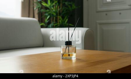 Ein stilvoller Reed-Diffusor auf einem Holztisch in einem modernen Wohnzimmer, mit weißem Sofa und üppig grünen Pflanzen, die eine ruhige und duftende Atmosphäre schaffen Stockfoto