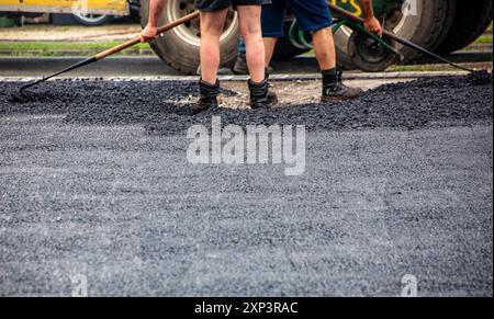 Arbeiter legen frischen Asphalt auf einer Straßenbaustelle ab und glätten die Oberfläche mit Rechen. Stockfoto