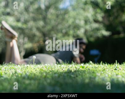 Eine Frau liegt auf dem Gras in einem Park. Das Gras ist grün und der Himmel blau Stockfoto