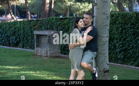 Mann und Frau umarmen sich in einem Park. Die Frau trägt ein grünes Kleid und der Mann trägt ein schwarzes Hemd und Shorts. Die Szene ist glücklich A Stockfoto