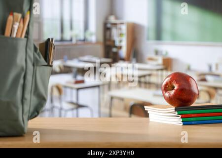 Schulsachen und Rucksack auf der Schulbank im Klassenzimmer. Verschwommener Hintergrund der Tafel an Wand und Fenster mit Sonnenlicht. Stockfoto