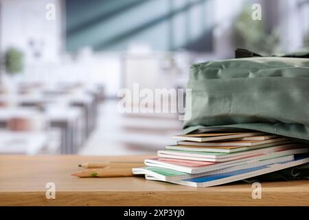 Schulsachen und Rucksack auf der Schulbank im Klassenzimmer. Verschwommener Hintergrund der Tafel an Wand und Fenster mit Sonnenlicht. Stockfoto
