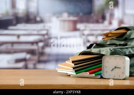 Schulsachen und Rucksack auf der Schulbank im Klassenzimmer. Verschwommener Hintergrund der Tafel an Wand und Fenster mit Sonnenlicht. Stockfoto