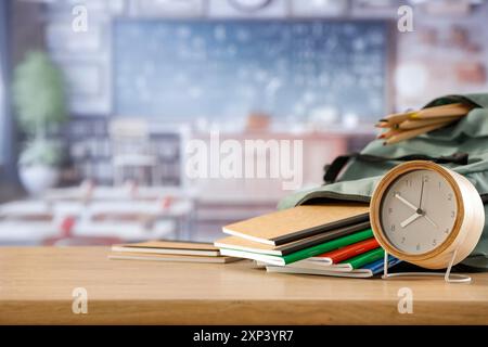 Schulsachen und Rucksack auf der Schulbank im Klassenzimmer. Verschwommener Hintergrund der Tafel an Wand und Fenster mit Sonnenlicht. Stockfoto