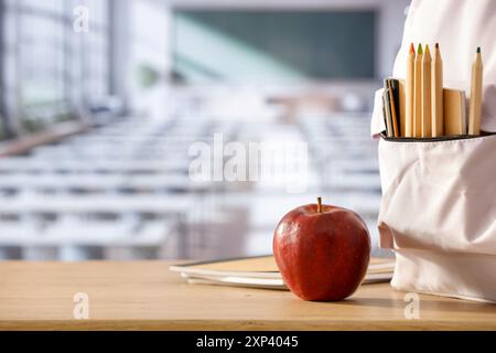Schulsachen und Rucksack auf der Schulbank im Klassenzimmer. Verschwommener Hintergrund der Tafel an Wand und Fenster mit Sonnenlicht. Stockfoto