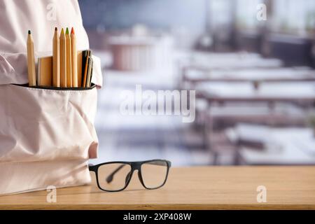 Schulsachen und Rucksack auf der Schulbank im Klassenzimmer. Verschwommener Hintergrund der Tafel an Wand und Fenster mit Sonnenlicht. Stockfoto