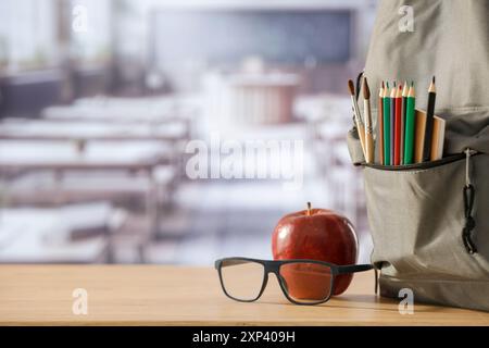 Schulsachen und Rucksack auf der Schulbank im Klassenzimmer. Verschwommener Hintergrund der Tafel an Wand und Fenster mit Sonnenlicht. Stockfoto
