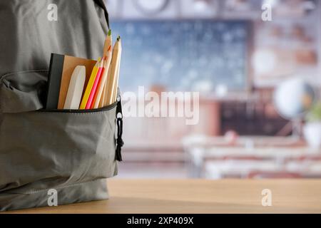 Schulsachen und Rucksack auf der Schulbank im Klassenzimmer. Verschwommener Hintergrund der Tafel an Wand und Fenster mit Sonnenlicht. Stockfoto