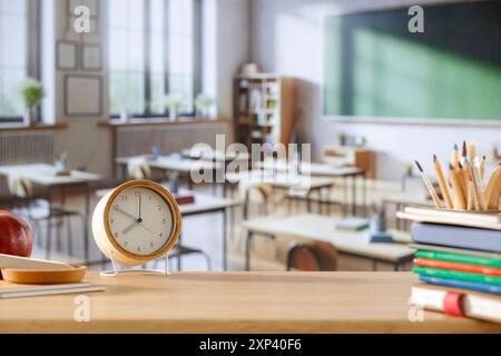 Schulsachen und Rucksack auf der Schulbank im Klassenzimmer. Verschwommener Hintergrund der Tafel an Wand und Fenster mit Sonnenlicht. Stockfoto
