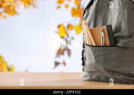 Schulrucksack und Schulsachen mit Platz für Produkte auf hölzernem Schreibtisch mit Herbstbaum und blauem Himmel Hintergrund. Zurück zur Schule. Kopierraum für Schule Stockfoto