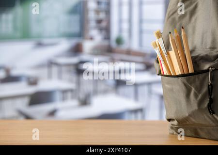 Schulsachen und Rucksack auf der Schulbank im Klassenzimmer. Verschwommener Hintergrund der Tafel an Wand und Fenster mit Sonnenlicht. Stockfoto