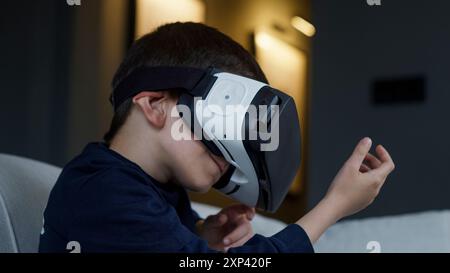 Ein kleiner Junge, der in die virtuelle Realität eingetaucht ist, ein VR-Headset trug und mit einer digitalen Umgebung interagierte. Begeisterung und Staunen der modernen Technologie AS Stockfoto