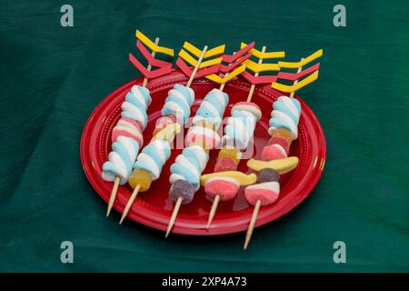 Süßwarenspieße auf leuchtend rotem Teller mit dekorativen Pfeilen, festlicher Tisch. Stockfoto