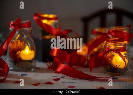 Kerzenlicht in Glasgläsern mit roten Bändern, ideal für festliche oder gemütliche Umgebungen Stockfoto