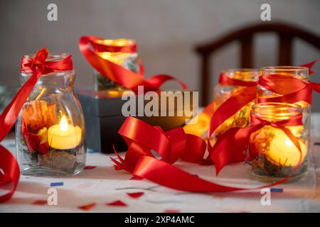 Warme Kerzen in Gläsern mit roten Bändern schaffen eine gemütliche festliche Atmosphäre. Stockfoto