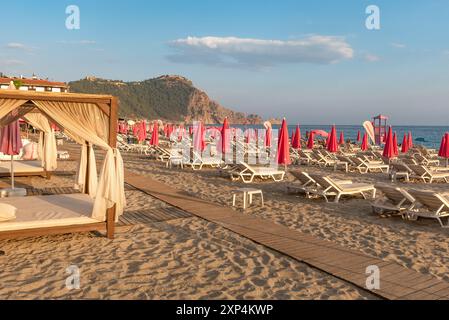 Alanya, Türkei. 9. Juli 2024 Sonnenliegen und rosafarbene Sonnenschirme am Cleopatra Beach im türkischen Ferienort Alanya an der Mittelmeerküste Stockfoto