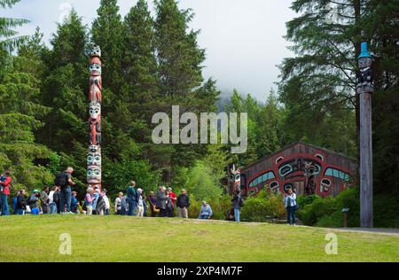 Eine Tourgruppe versammelt sich in der Nähe von zwei der 25 Pole im Saxman Totem Park in der Nähe von Ketchikan. Stockfoto