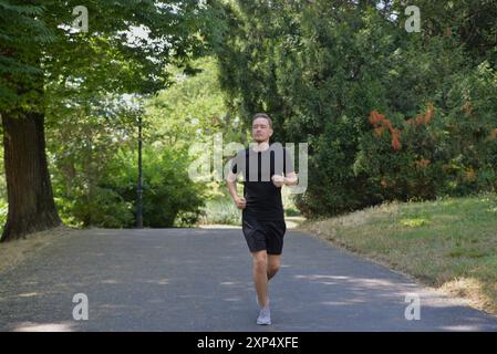Ein Mann, der in einem Park joggt. Ein junger Mann, der an einem Sommertag draußen läuft. Das Konzept von Flüchtigkeit, Training und gesundem Lebensstil. Stockfoto