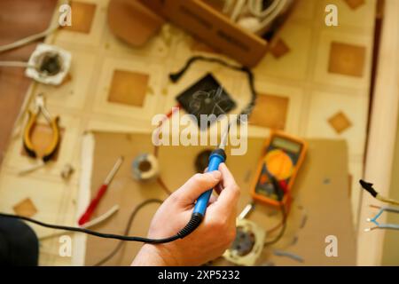 Lötkolben im Einsatz, mit Rauch und Verkabelung auf einer Werkbank, Draufsicht, ideal für Reparaturanleitungen, elektrische Arbeitsanleitungen und DIY-Projektblogs Stockfoto