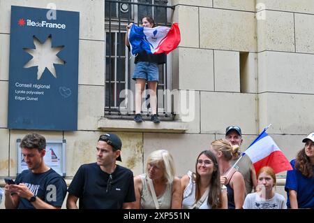 Paris, Frankreich. August 2024. Ein junges Mädchen winkt eine französische Flagge von einem Fenstervorsprung in der Rue des Martyrs. Quelle: SOPA Images Limited/Alamy Live News Stockfoto