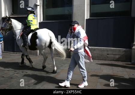 Manchester, England, Großbritannien. August 2024. Ein Befürworter einer strengeren Einwanderung spricht am Telefon nicht über einen Polizisten zu Pferd, der versucht, die Demonstranten im Zentrum von Manchester zu kontrollieren. Nach der Ermordung von drei Kindern in Stockport sehen mehr als ein Dutzend Städte Demonstrationen und antirassistische Gegendemos in ganz Großbritannien. Bei einigen Versammlungen gab es Unruhe. Ein 17-jähriger Mann wurde verhaftet und wegen Mordes angeklagt (Credit Image: © Martin Pope/ZUMA Press Wire). Nicht für kommerzielle ZWECKE! Stockfoto