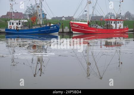 Zwei alte, historische Garnelenboote im malerischen Hafen, teilweise gefroren, im Fischerdorf Greetsiel in der kalten Januarzeit. Deutschland. Stockfoto