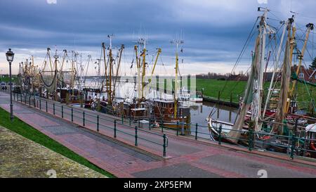 Gesamtansicht: Malerischer Hafen, teilweise gefroren, im Fischerdorf Greetsiel mit alten Garnelenbooten in der kalten Januarzeit. Ostfriesland Stockfoto