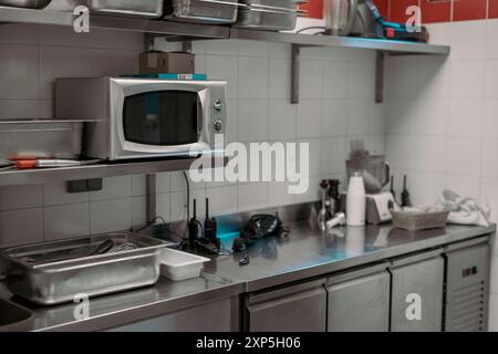 Küchenutensilien, Pfannen und Töpfe in einer professionellen Küche. Industrielle Hardware in einer Restaurantküche. Konzentrieren Sie sich auf die Mikrowelle. Stockfoto