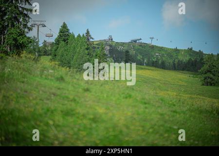 Skipiste Nassfeld im Sommer. Sichtbare obere Seilbahnstation und Gondelstation mit Blick auf grüne Wiesen unter blauem Himmel. Alpenpanorama in Summe Stockfoto