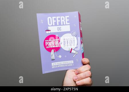 Paris, Frankreich - 1. April 2024: Eine männliche Hand, die einen Flyer mit einem Sonderangebot für Hörgeräte mit einem deutlich dargestellten Preis von 0 hält, der ein kostenloses Angebot vor neutralem Hintergrund anzeigt Stockfoto