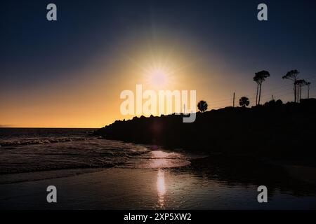 Sonnenuntergang mit Lichtstrahlen, die auf nassem Sand und Rock Jetty am Cape San Blas, Florida, USA, reflektieren Stockfoto