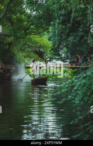 Suzhou, China - 11. Juni 2024 : Ein Mann rudert ein kleines Boot über einen ruhigen Teich im Garten des bescheidenen Administrators in Suzhou, China. Stockfoto