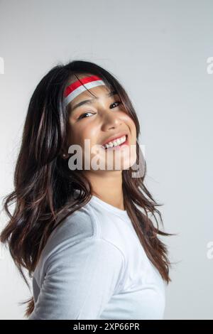 Nahaufnahme einer schönen asiatischen Frau in weißem T-Shirt lächelt und schüttelt ihr langes Haar isoliert auf weißem Hintergrund Stockfoto