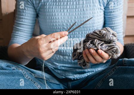Frau in blauer Kleidung, die einen Ball aus grauem Garn und Stricknadeln hält. Mädchen, das mit gewebten Fäden und Nadeln in den Händen sitzt. Strickkonzept. Stockfoto