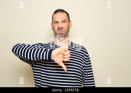 Bärtiger hispanischer Mann, der 40er Jahre in lässiger Kleidung trug, sah unglücklich und wütend aus, zeigte Ablehnung und Negativität mit Daumen nach unten Geste. Schlecht Stockfoto